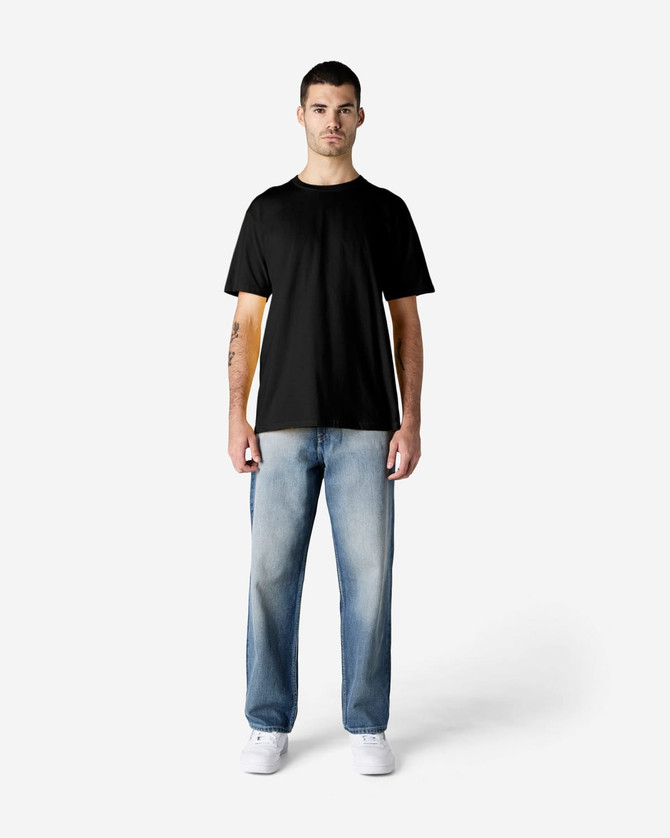 A black Gildan Softstyle adult t-shirt on a male model, paired with light blue jeans and white shoes.