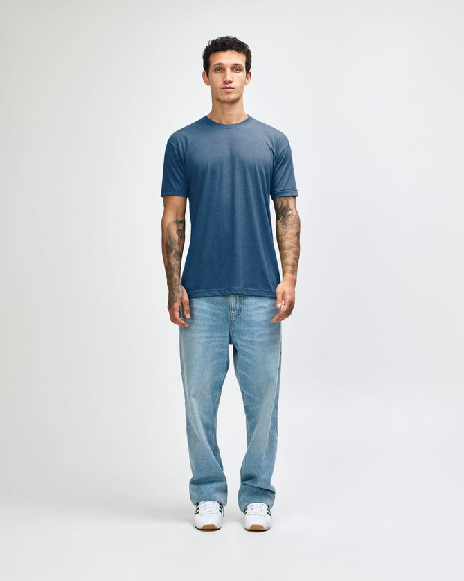 A man wearing a blue American Apparel Tri-Blend T-Shirt paired with light blue jeans and white sneakers.