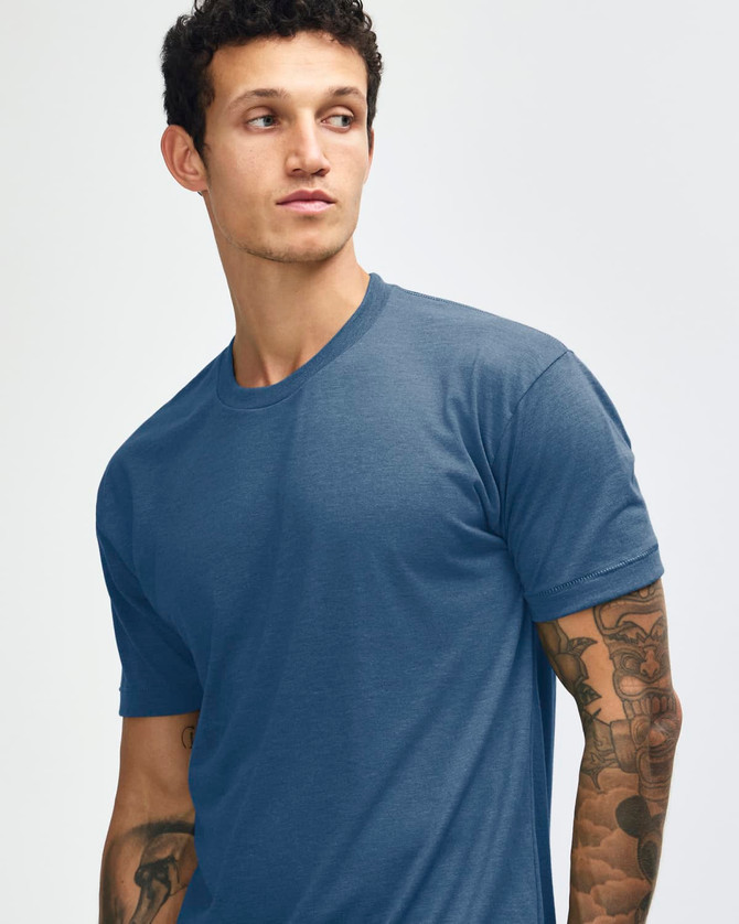A blue American Apparel tri-blend t-shirt worn by a person with tattoos. The shirt has a round neck and short sleeves.