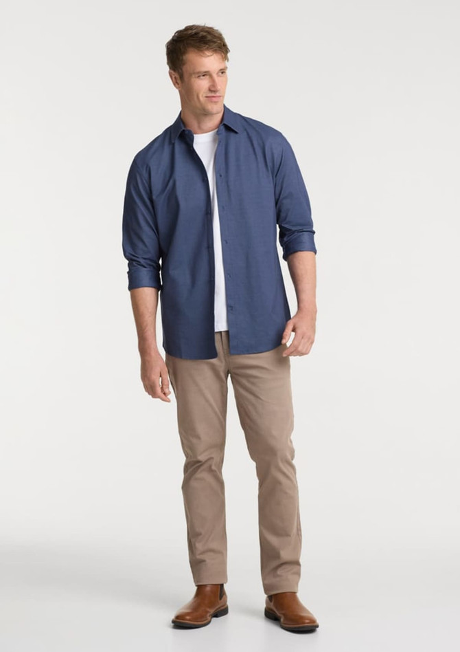 A man wears a navy long sleeve shirt with rolled sleeves, paired with light tan pants and brown boots.