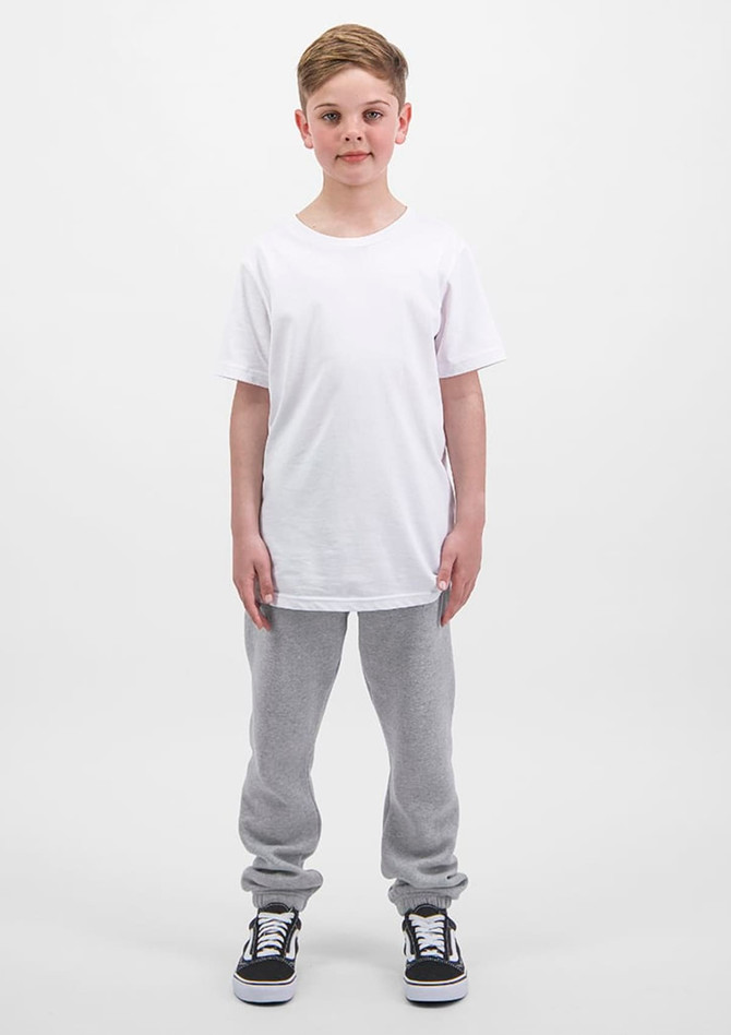 A child stands upright, wearing a plain white t-shirt and grey track pants, with black and white sneakers.