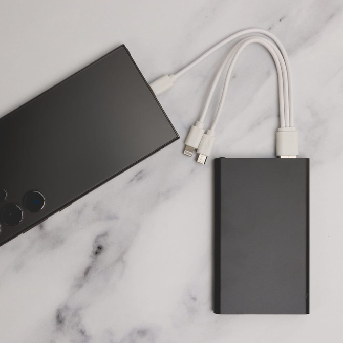 A black power bank with charging cables connected, resting on a marble surface.