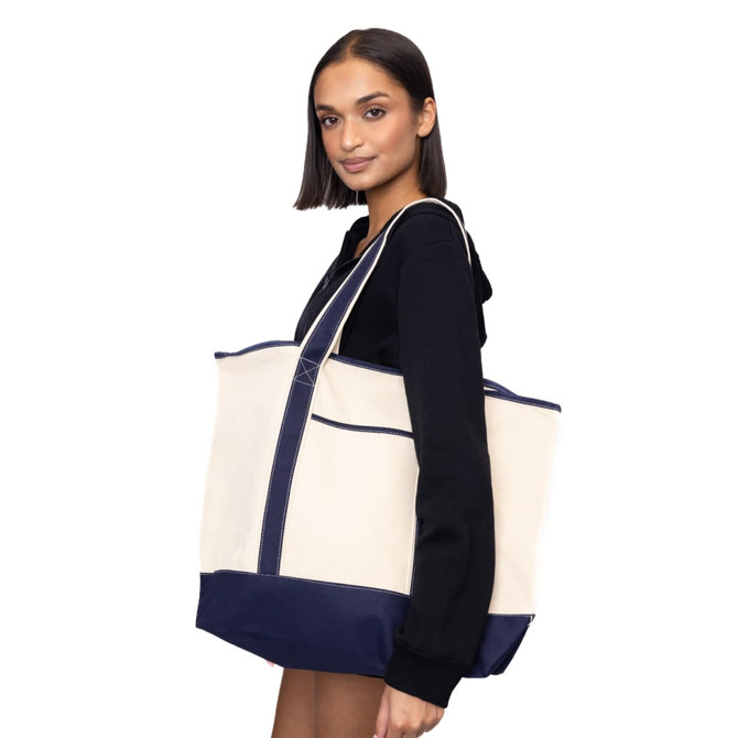 A model holds a large beige and navy tote bag with a sturdy design and visible branding.