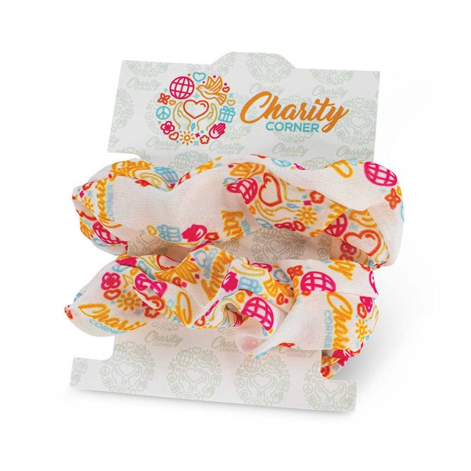 A set of two fabric hair scrunchies in vibrant colours featuring floral and abstract patterns, on a branded card.