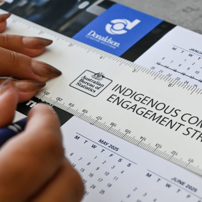 A ruler featuring a light colour with text, being held above a calendar on a table surface.
