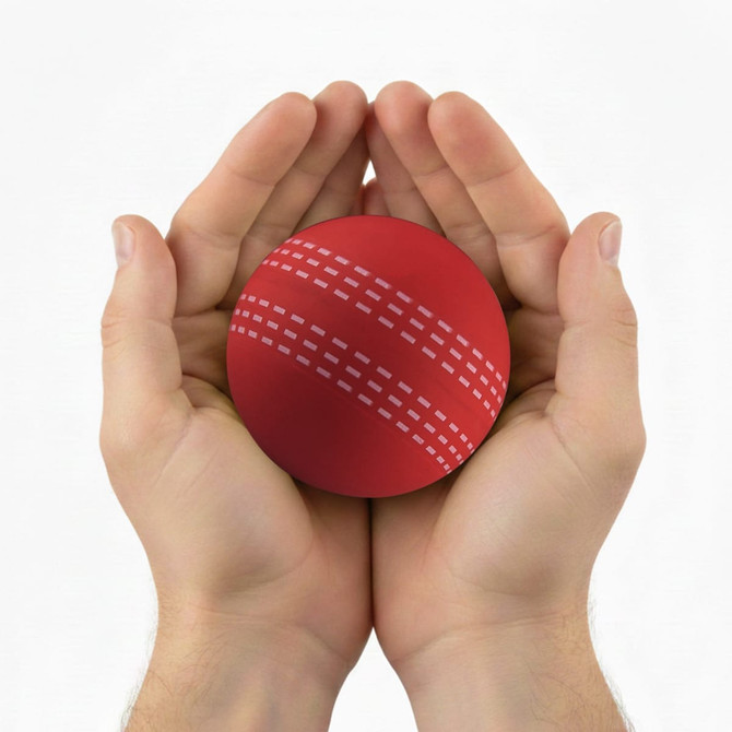 A red cricket ball held gently in two hands, featuring distinctive seam markings. The image has a logo.