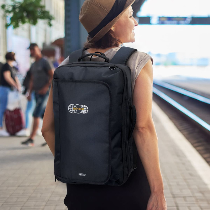 A black convertible travel backpack with a logo, worn by a woman at a train station.