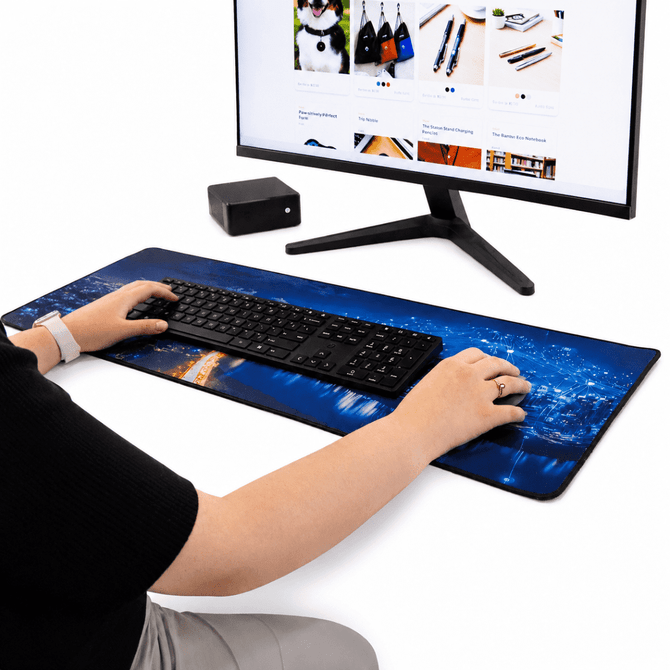 A desk mat featuring a blue city skyline design, with a keyboard and hands positioned on it, next to a monitor.