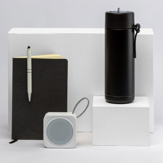 A black drink bottle, a black notebook, a white speaker, and a pen arranged on white pedestals. All products have branding.
