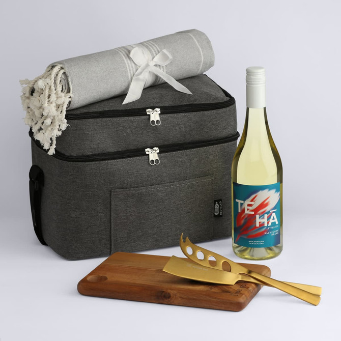 A cooler bag in grey with a blanket, a bottle of white wine, a wooden cutting board, and gold utensils.