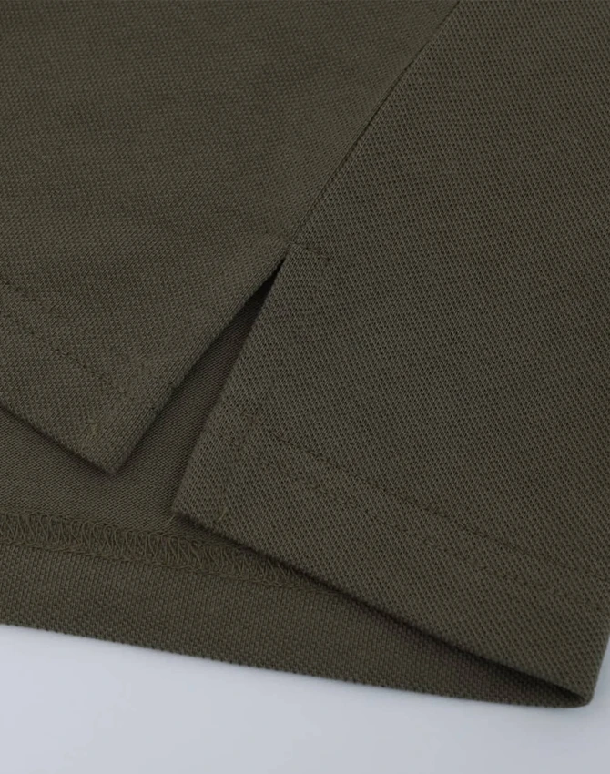 A close-up of a short-sleeved polo in an olive green cotton/poly pique fabric with a stitched hem.