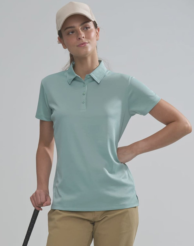 A woman wearing a light blue polo shirt and a beige cap stands with a golf club in hand. The image features a logo on the shirt.