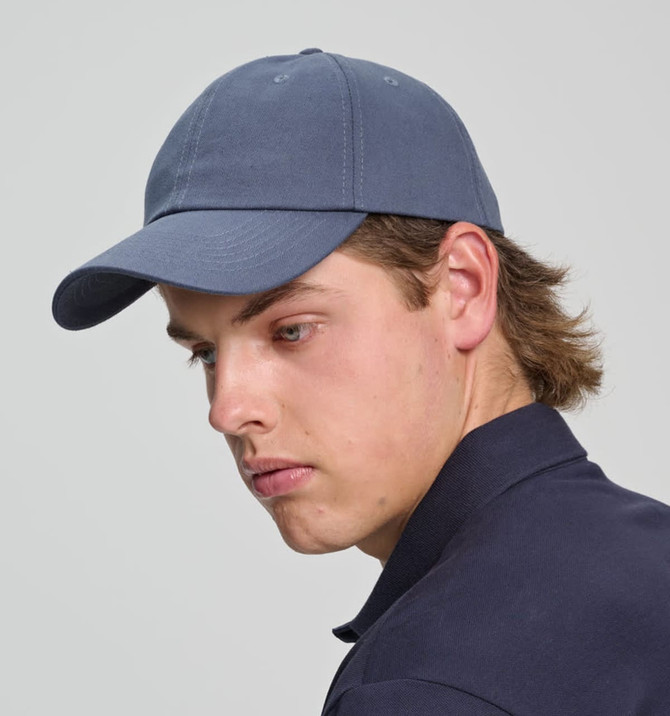 A cotton twill unstructured cap in navy blue, worn by a model with light brown hair. The cap has a logo.