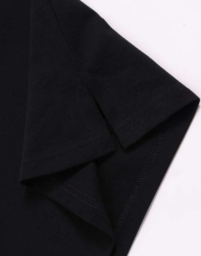 A black ultrafine cotton pique polo featuring a folded sleeve, with a small logo on the fabric.