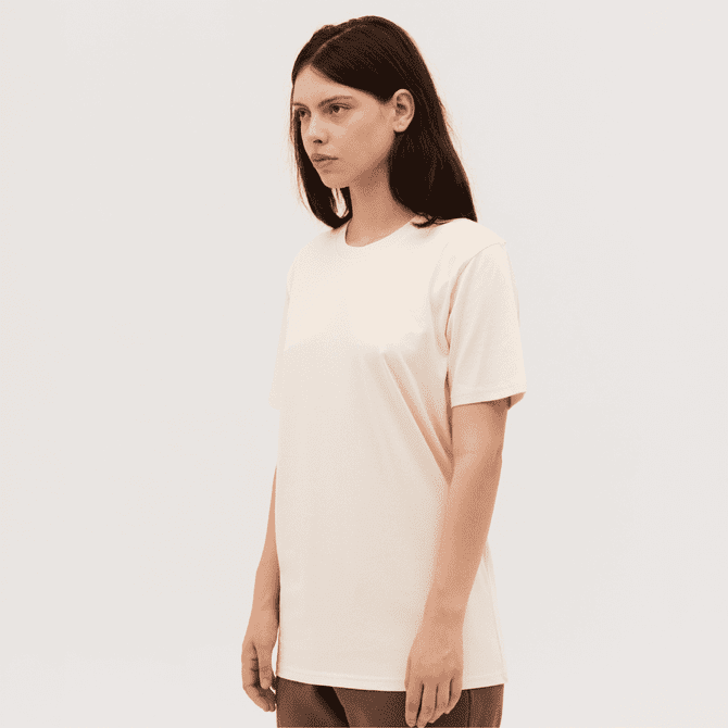 A plain light peach Classic Tee displayed on a model standing against a neutral background. The tee has a simple design and a logo.