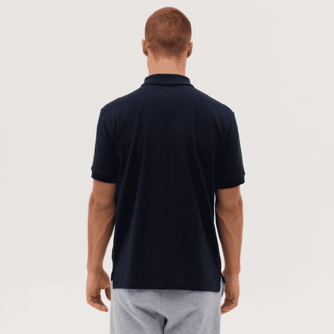 A navy polo shirt with a collar, viewed from the back. The model has short hair and is wearing grey shorts.