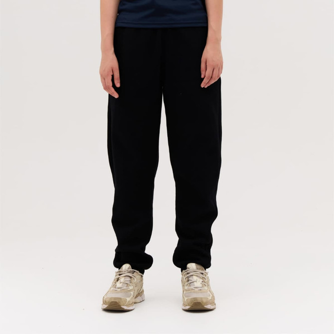 Black track pants with a relaxed fit, paired with beige shoes. The model stands against a plain background.