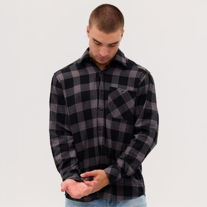A man wearing a black and grey checkered flannel long sleeve shirt with a pocket, adjusting his cuff.