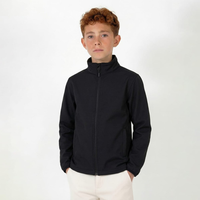 A youth's softshell jacket in black, featuring a zip-up front and a high collar. The model is standing and looking at the camera.