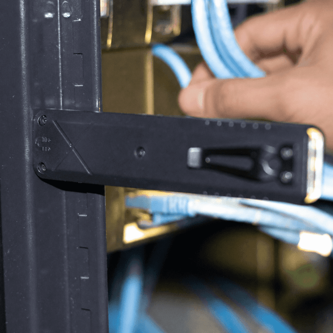 A black tool with a handle and measurement markings, positioned near blue cables in a rack.