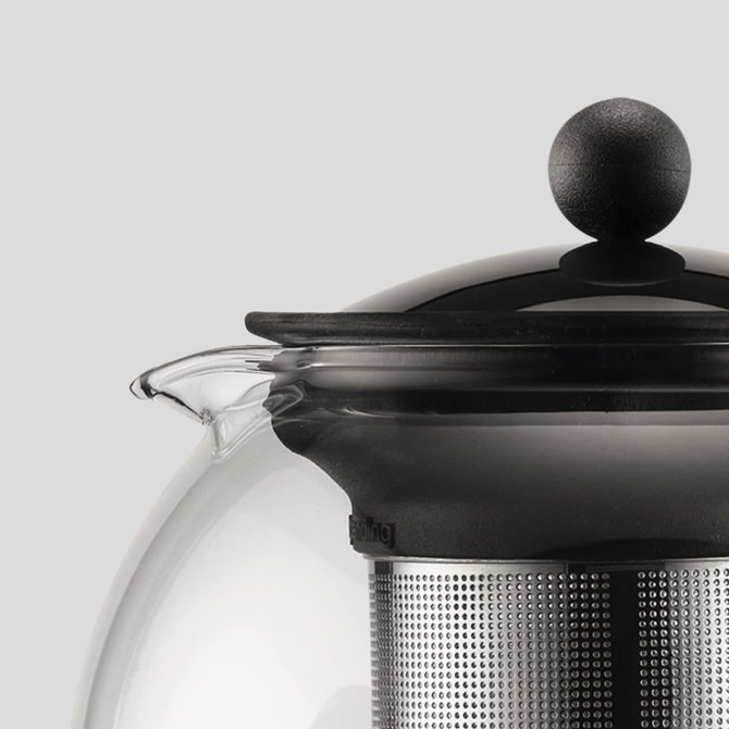A black and silver tea press with a rounded glass body and a large round knob on the lid, featuring a stainless steel infuser.