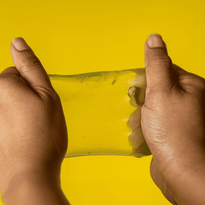 A pair of hands stretching a translucent yellow jelly cube sensory toy against a bright yellow background.