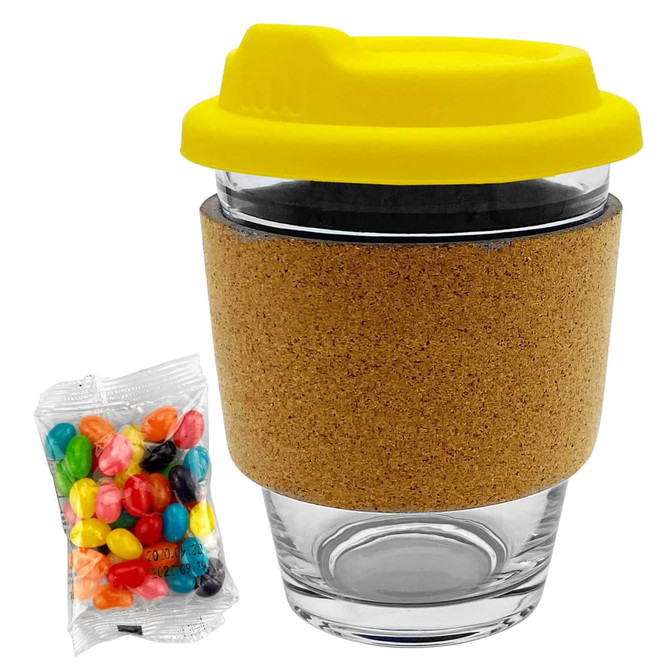 A glass coffee cup with a cork band and a yellow lid, accompanied by a pack of colourful jelly beans.