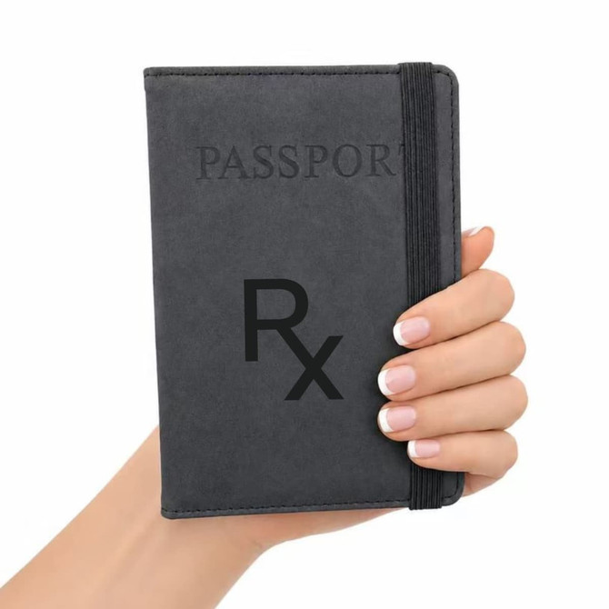 A grey passport wallet is held in a hand, featuring a band for secure closure and a logo on the cover.