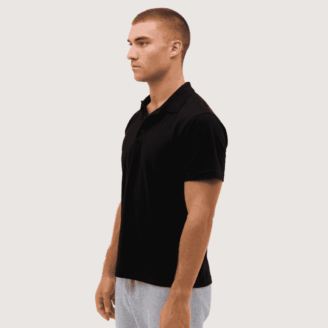 A black polo shirt is displayed on a model standing sideways, featuring a subtle logo on the chest.