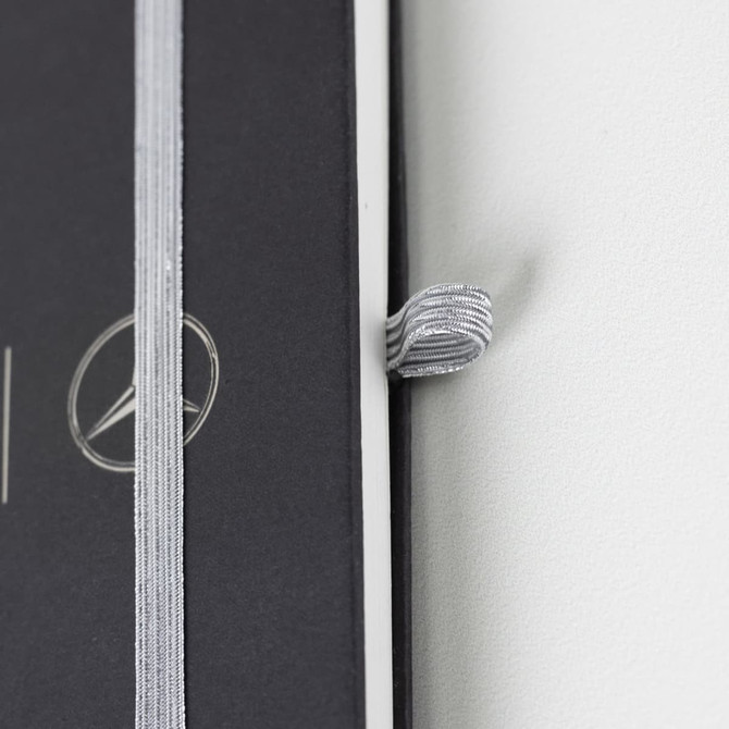 A black A5 notebook with a silver elastic band and a logo on the cover.