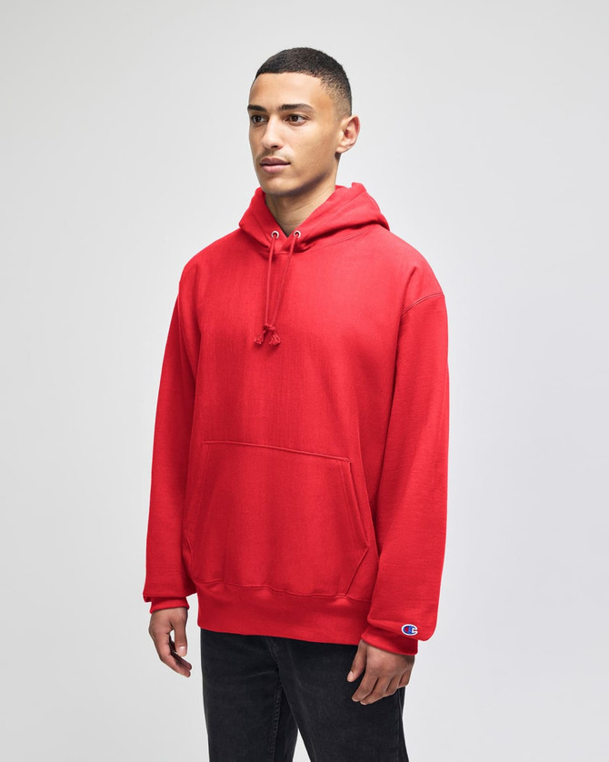 A red pullover hooded sweatshirt with a front pocket and logo on the sleeve, displayed on a model.