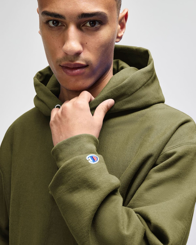 A man in a green hooded sweatshirt, featuring a logo on the sleeve and a focused expression.