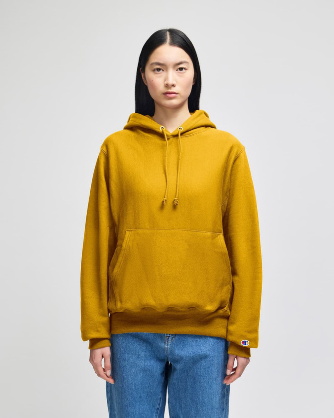 A mustard yellow pullover hooded sweatshirt with a front pocket and a logo on the sleeve.