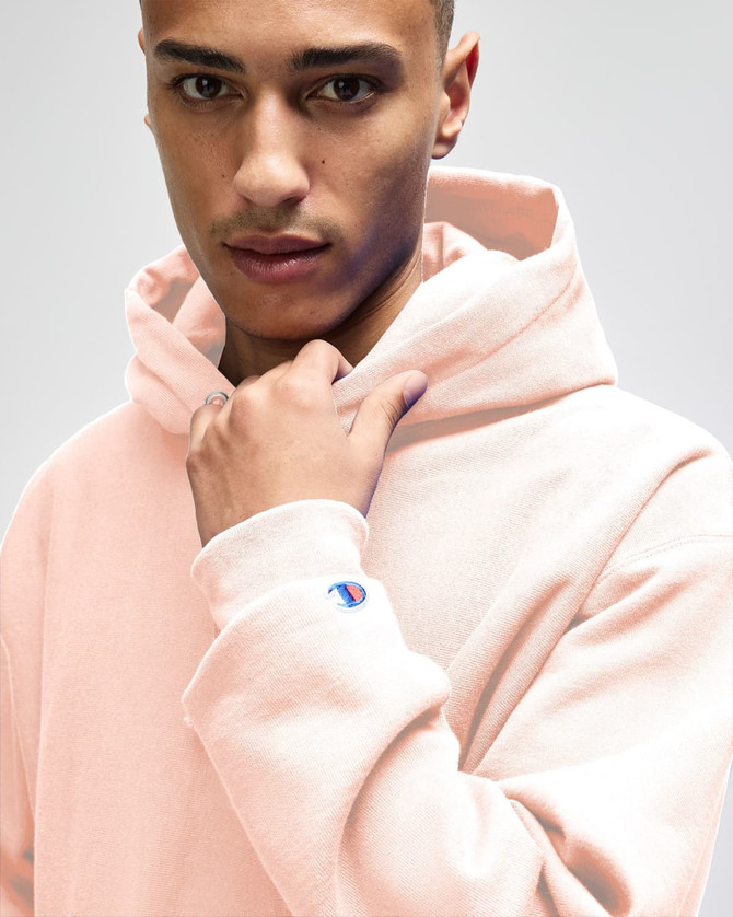 A model wearing a pink Champion Reverse Weave® adult pullover hooded sweatshirt with a visible logo on the sleeve.