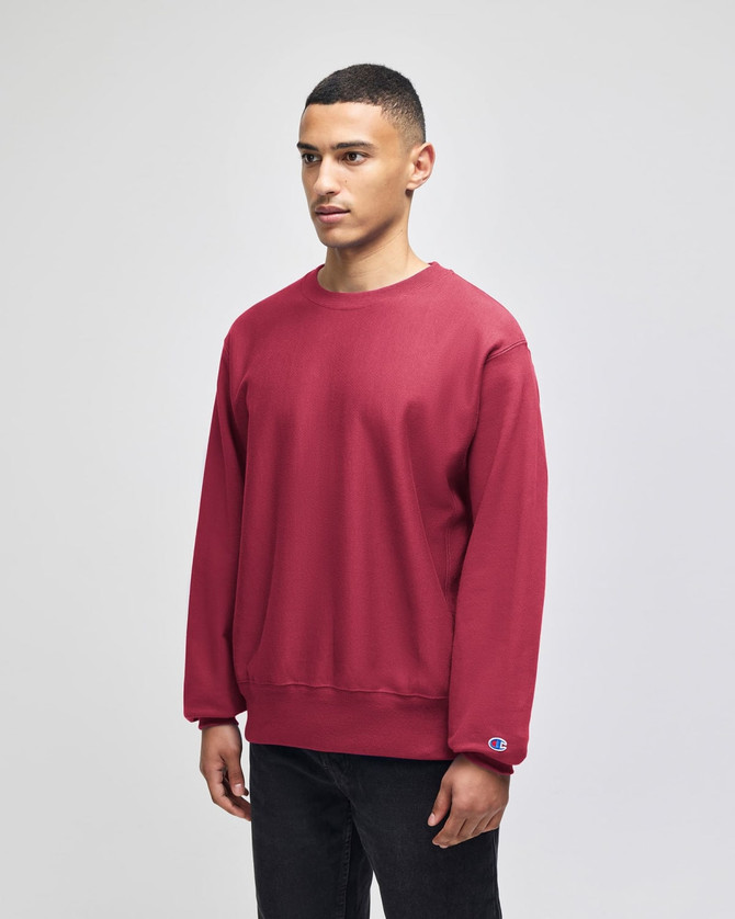 A red sweatshirt with a loose fit and a logo on the sleeve, worn by a model standing upright.