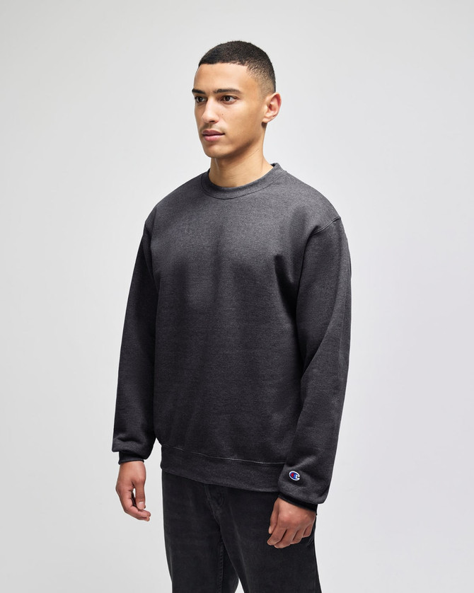 A grey crewneck sweatshirt on a model, featuring a logo on the sleeve and a relaxed fit.