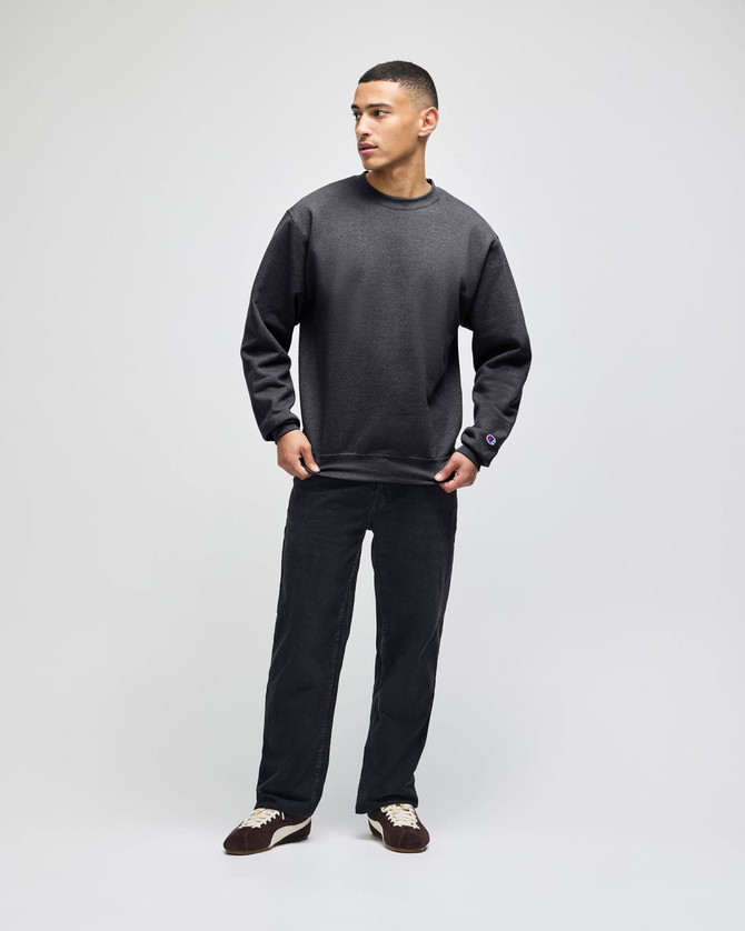 A man wearing a dark grey Champion Powerblend® adult crewneck sweatshirt paired with black pants.