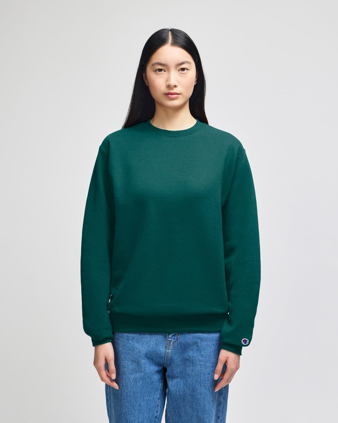 A green crewneck sweatshirt with a logo, displayed on a model wearing blue jeans.