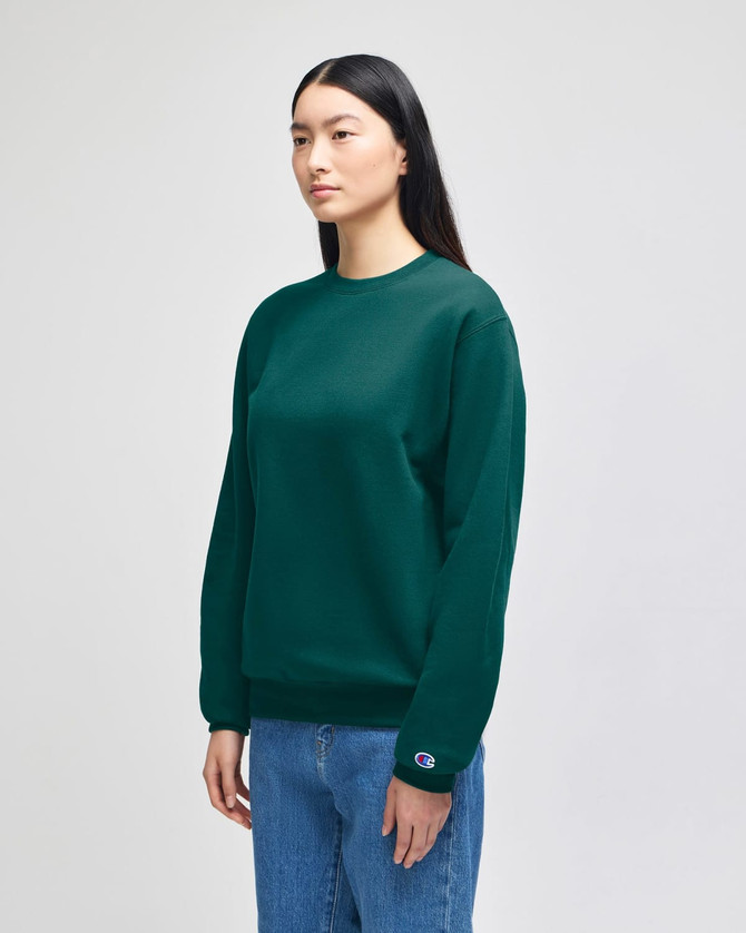 A green crewneck sweatshirt with a logo, worn by a model standing in front of a neutral background.