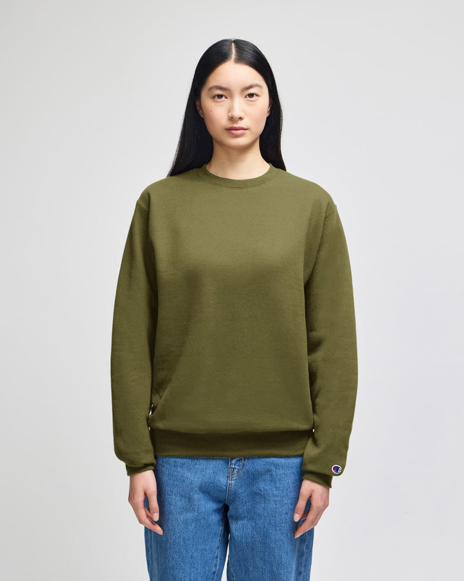 An adult crewneck sweatshirt in olive green, featuring a logo and styled with blue jeans.