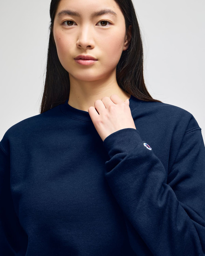 A woman wearing a navy blue crewneck sweatshirt featuring a logo on the sleeve.