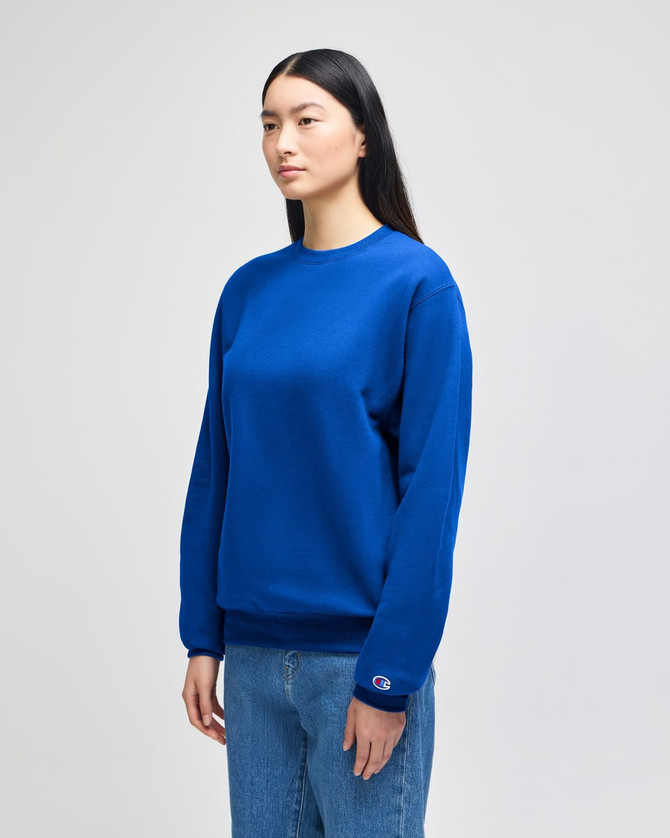 A blue crewneck sweatshirt on a model, featuring long sleeves and a logo on the cuff.