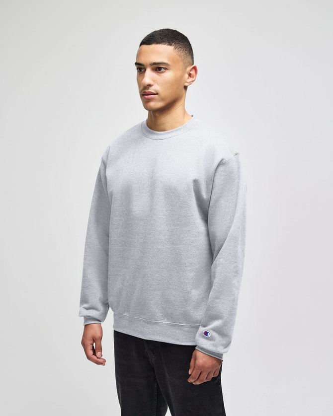 A grey Champion Powerblend® adult crewneck sweatshirt on a model, featuring a logo on the sleeve.