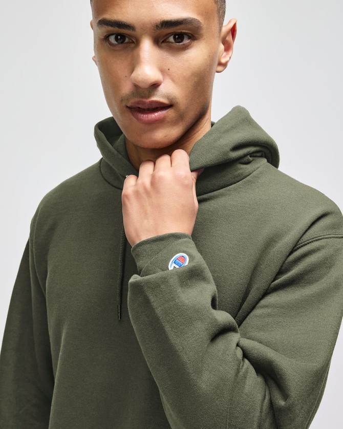 A green hooded sweatshirt with a fitted design and a small logo on the sleeve, worn by a model.