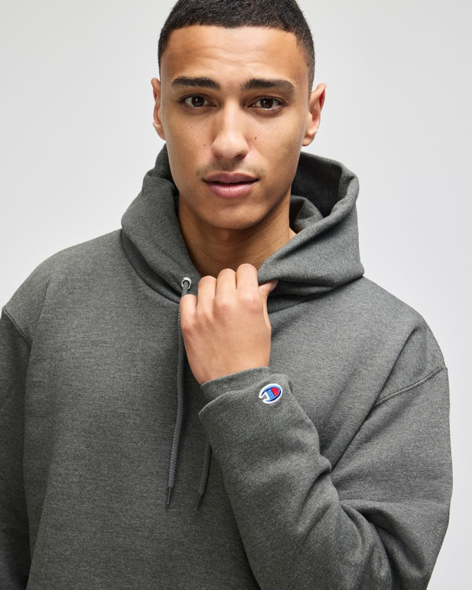 A grey pullover hooded sweatshirt on a model, featuring a logo on the sleeve.