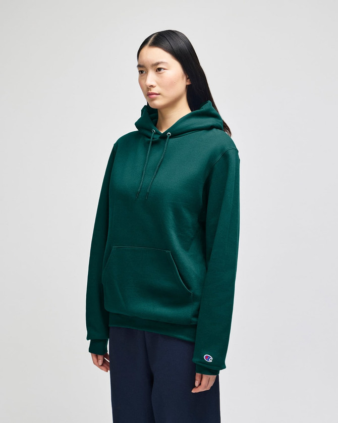 A green hooded sweatshirt with a front pocket and a logo on the sleeve, modelled by a woman.