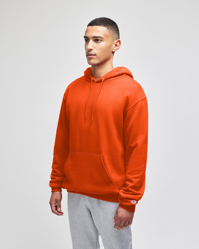 An orange pullover hooded sweatshirt with a front pocket and a logo on the sleeve. Styled with grey bottoms.