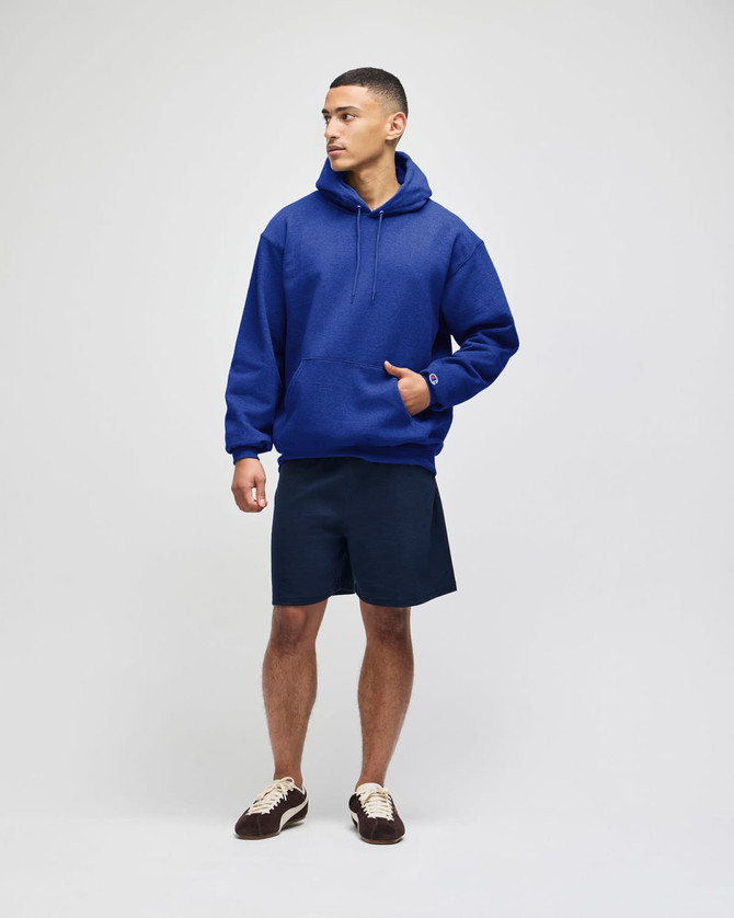 A blue pullover hooded sweatshirt worn by a model, paired with navy shorts and featuring a logo.