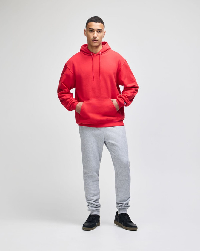 A red pullover hooded sweatshirt worn with grey sweatpants, featuring a front pocket and a logo.