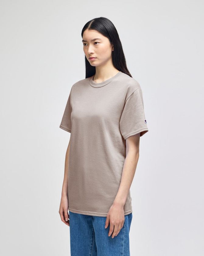A plain beige adult short-sleeve t-shirt displayed on a model, featuring a logo on one sleeve.